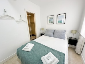 Quarto de hotel com cama, duas mesas de cabeceira, chuveiro, porta e duas imagens emolduradas na parede.