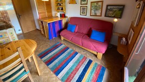 Un salon chaleureux avec un plafond en bois, un canapé rouge agrémenté de coussins bleus, un tapis à rayures et des meubles en bois.