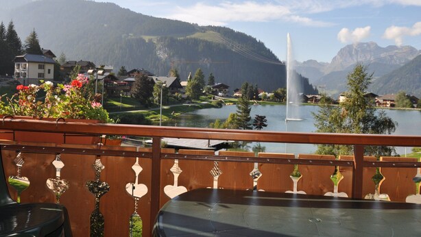 Un balcon avec vue sur un lac, des montagnes et une fontaine.
