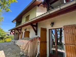 A two-story building with a stone-paved patio, wooden doors, and a covered outdoor seating area.