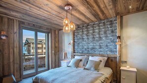 A bedroom with a wooden ceiling, a large bed with a fluffy rug, and a view of a building through a glass door.