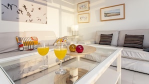 Ein modernes Wohnzimmer mit einem Glastisch, zwei orangefarbenen Getränken, dekorativen Kugeln und einem Wandbild mit Vögeln.