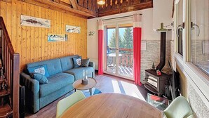 Um quarto aconchegante com teto de madeira, um sofá azul, uma pequena mesa redonda e uma lareira a lenha.