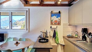 Uma cozinha compacta com área de refeições, uma janela com vista para as montanhas e um cartaz na parede.