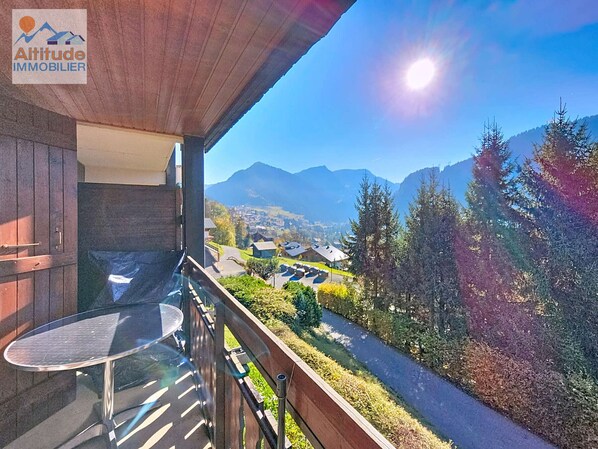 A balcony with a glass table and chairs, overlooking a scenic mountain view with a clear sky.