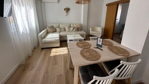 Una sala moderna con un sofá, una mesa de comedor con individuales, una lámpara colgante y un aire acondicionado de pared.