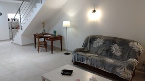 A living room with a sofa, a coffee table, a desk with a chair, a lamp, and a staircase leading to a bookshelf.