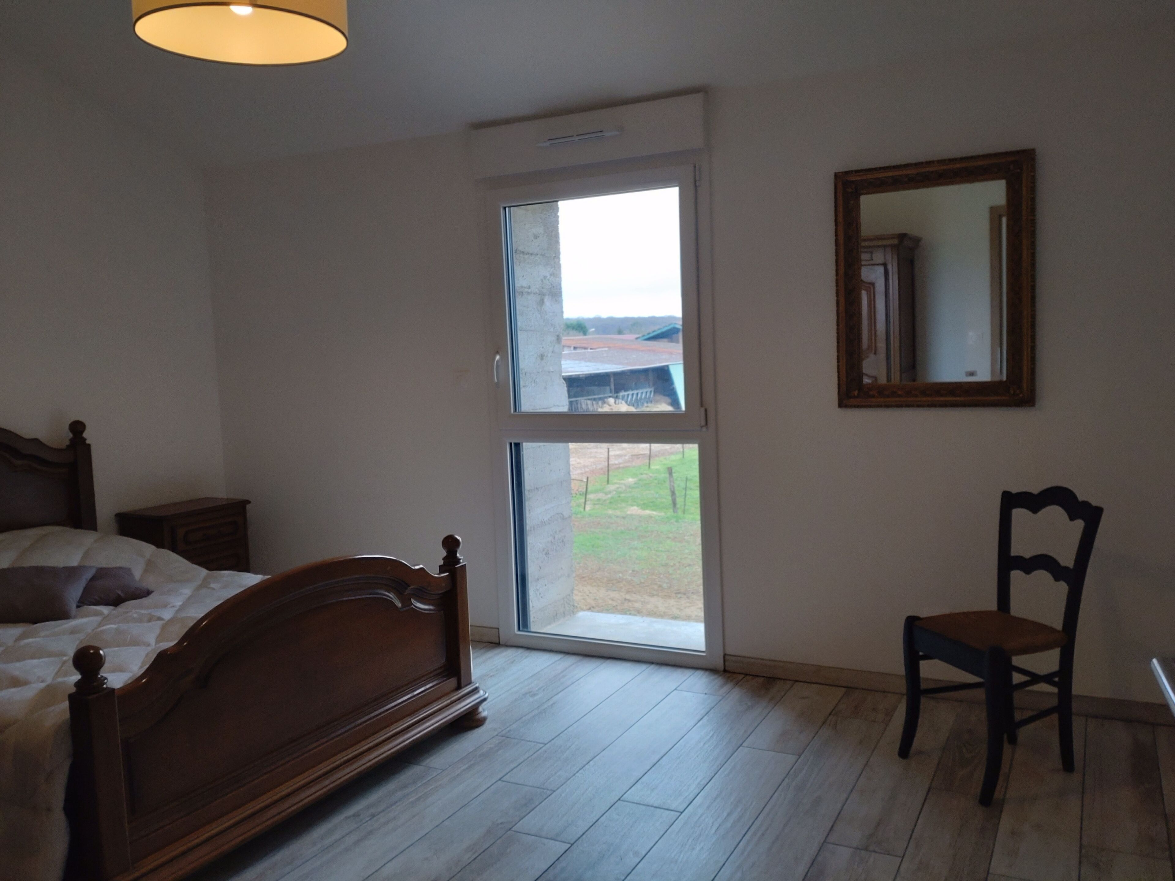 Un dormitorio con cama de madera, una silla, un ventanal y un espejo.