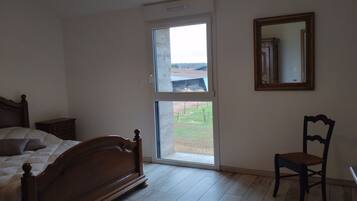 Un dormitorio con cama de madera, una silla, un ventanal y un espejo.