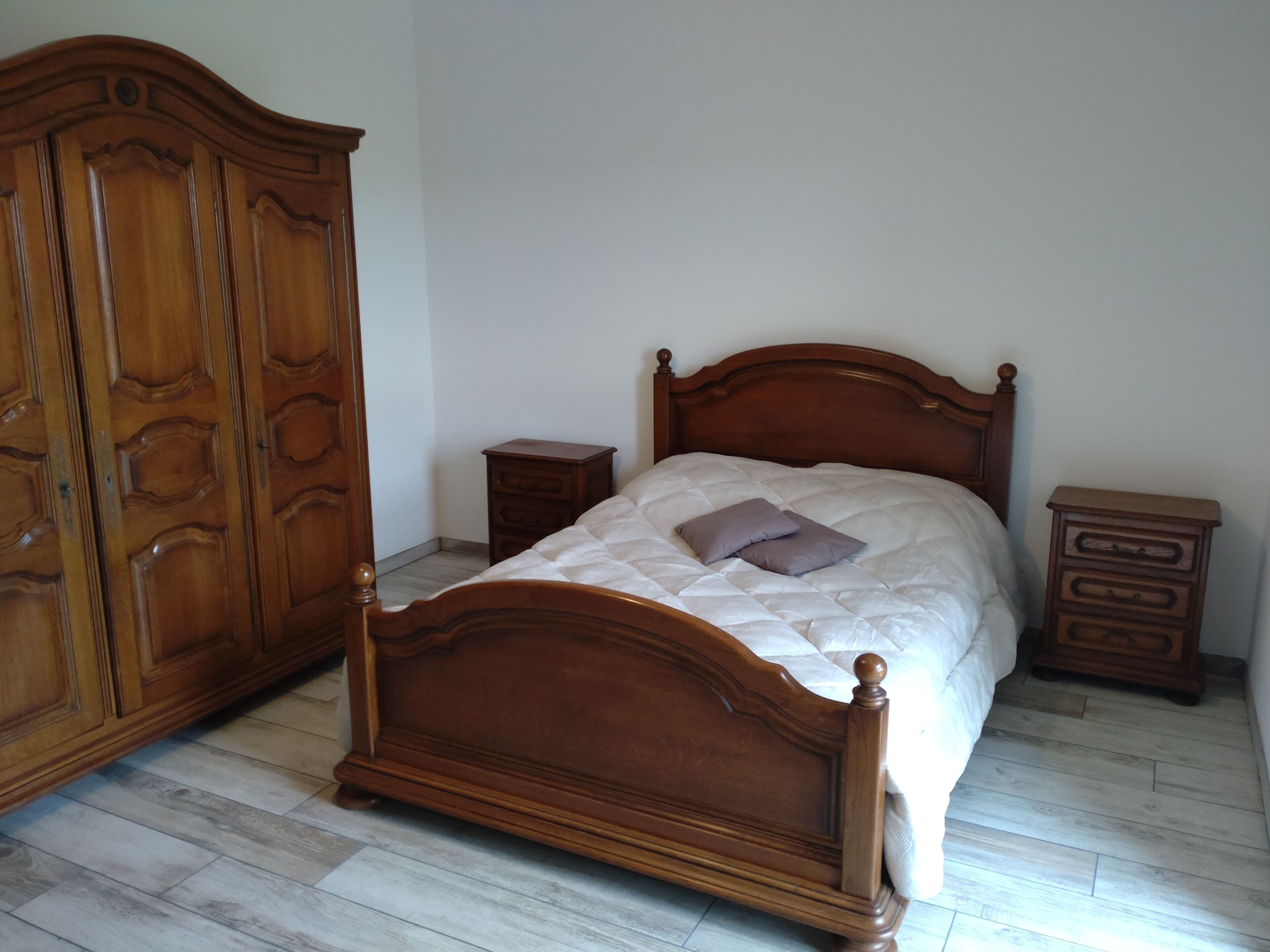 Une chambre à coucher avec un lit en bois, une table de chevet, une commode et une armoire.