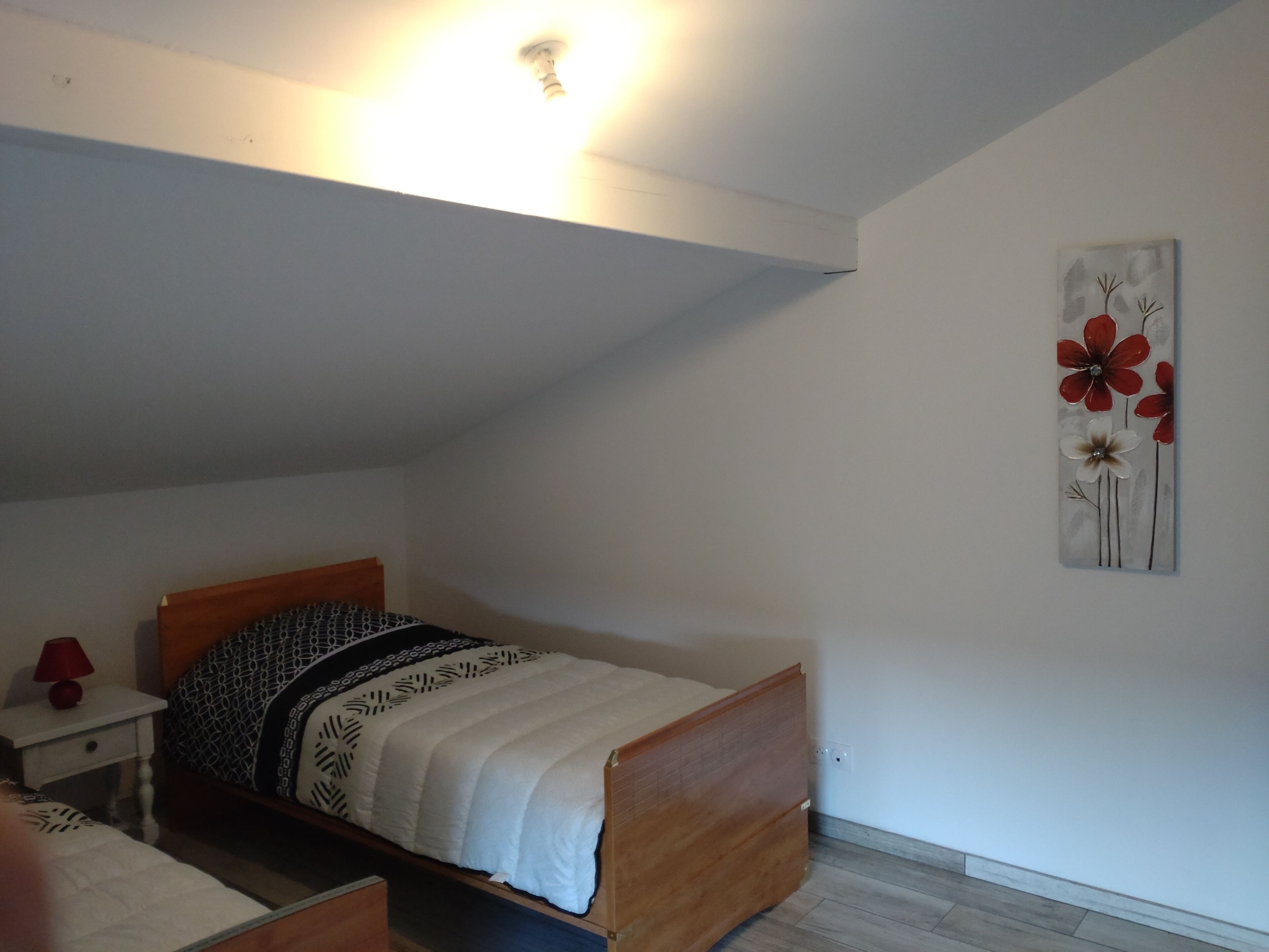 Een slaapkamer met een eenpersoonsbed, een nachtkastje, een lamp en een kunstwerk aan de muur.