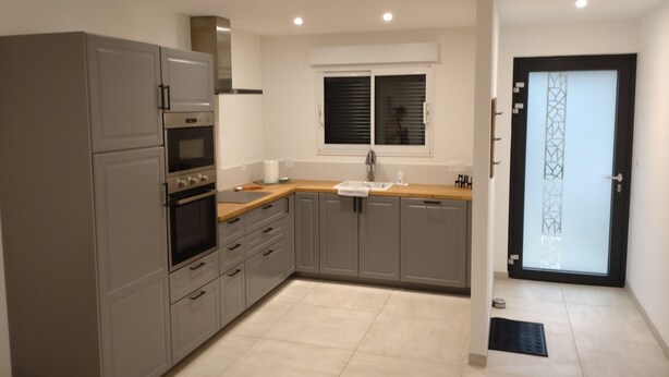 A modern kitchen with grey cabinets, a built-in oven, and a window with blinds.