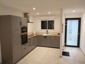 Une cuisine moderne avec des meubles gris, un four encastré et une fenêtre équipée de stores.