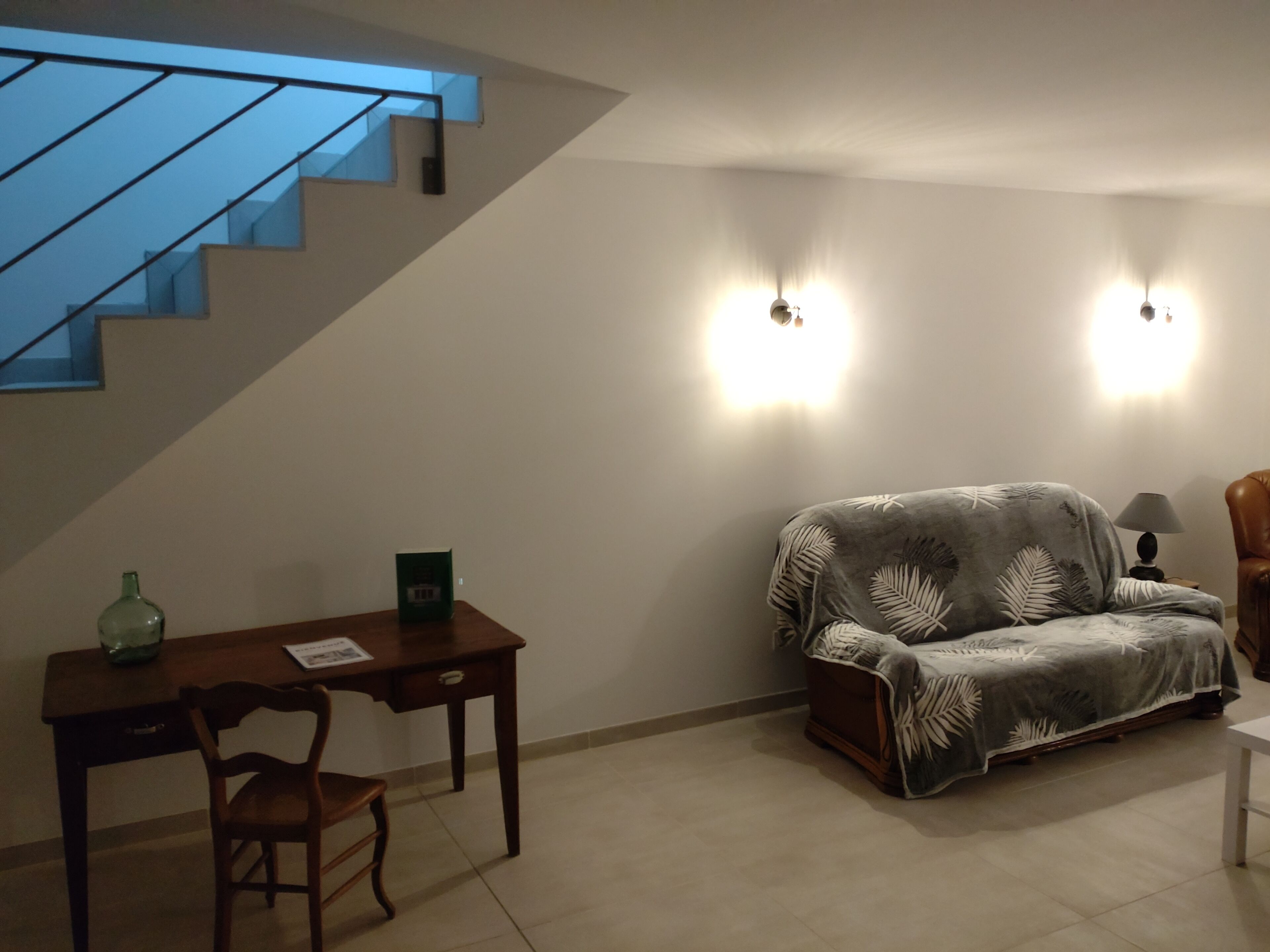 Ein Wohnzimmer mit einer Couch, einem Holztisch und einem Sessel. Eine Treppe mit blauen Geländern führt zu einer oberen Ebene.