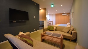 A modern living room with a flat-screen TV mounted on the wall, a glass coffee table, and two sofas with cushions.