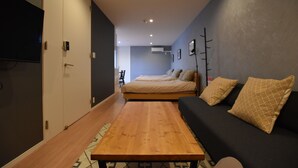 A compact room with a bed, a sofa, a wooden table, and a TV mounted on the wall.