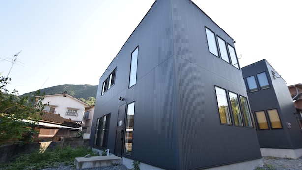 A modern two-story building with a sloped roof, large windows, and a gravel driveway.