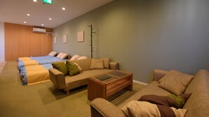 A modern hotel room with a sofa, a glass coffee table, a bed with blue bedding, and a wooden floor.