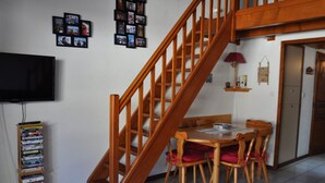 Una escalera que lleva a un nivel superior, una mesa de comedor con sillas, un televisor y un estante con DVD.