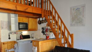 Cocina compacta con armarios de madera, microondas y pileta. En la sala de estar, un sofá de cuero negro con almohadones estampados.