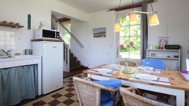 A kitchen with a microwave, sink, and a dining area with wicker chairs and a table set for two. - Typical house with enclosed garden in the heart of Cotentin (Saint-Jean-de-la-Rivière)