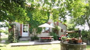 A rustic outdoor seating area with a table and chairs, surrounded by lush greenery and a brick wall. - Typical house with enclosed garden in the heart of Cotentin (Saint-Jean-de-la-Rivière)