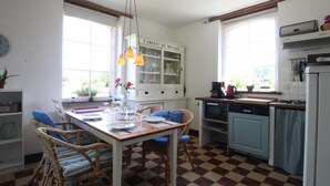 A kitchen with a checkered floor, a dining table with chairs, a cabinet labeled "CABINET DE MENAGE", and a window with a view of greenery. - Typical house with enclosed garden in the heart of Cotentin (Saint-Jean-de-la-Rivière)