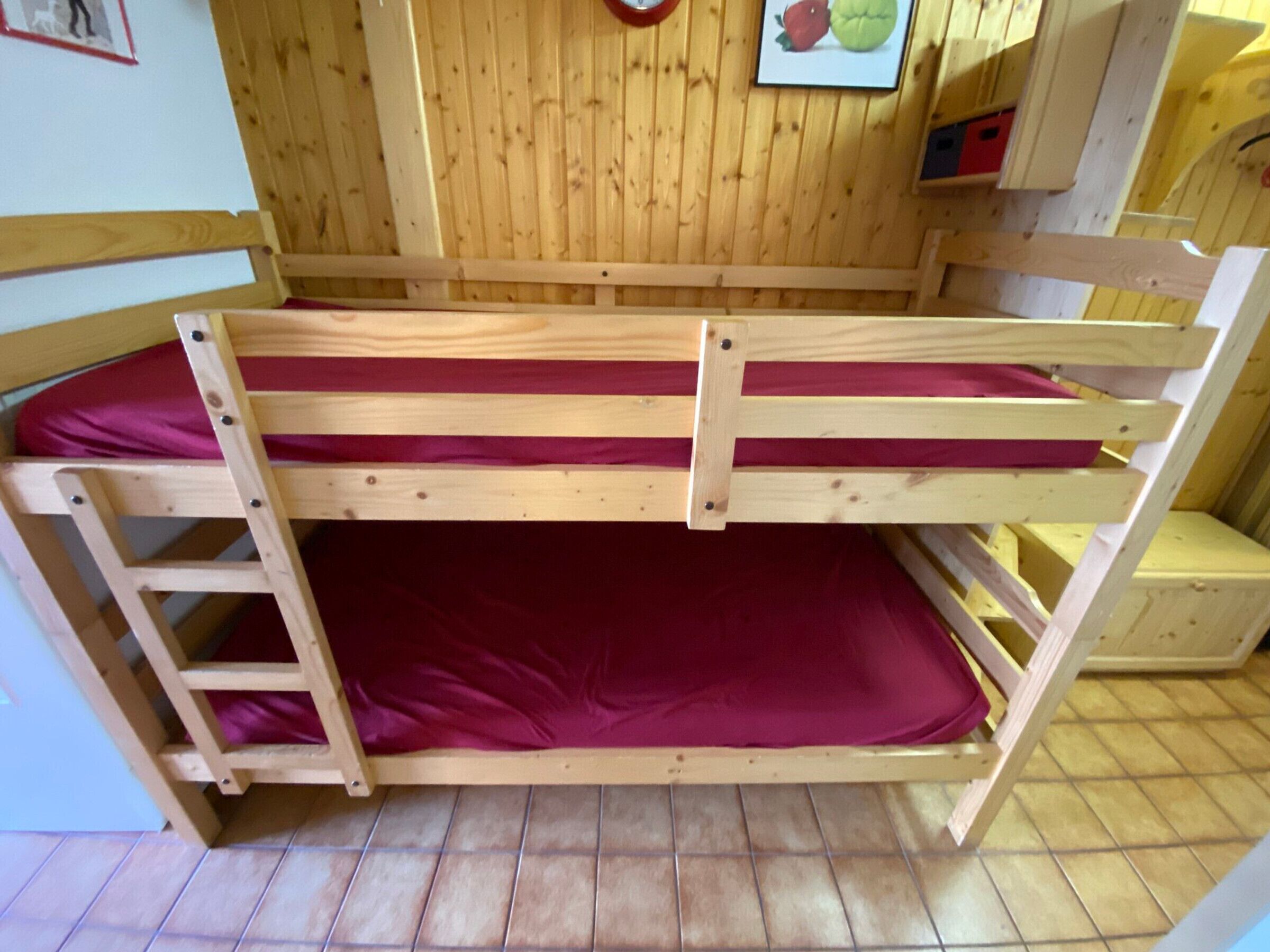 A bunk bed with a ladder, wooden walls, and a tiled floor.