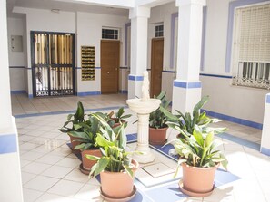 Une cour avec des plantes en pot, une fontaine et une porte.