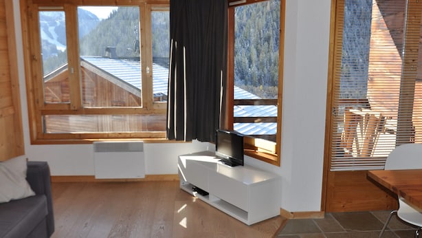 A modern living room with a large window, wooden ceiling, and a flat-screen TV on a white stand. - Charming studio in Châtel, near center, parking included (Châtel)