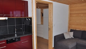 A compact kitchen with red cabinets and a black countertop, a gray sofa with pillows, and a wooden ceiling. - Charming studio in Châtel, near center, parking included (Châtel)