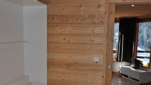 A bedroom with a wooden wall, a bed, a TV on a white stand, and a window with a view of trees. - Charming studio in Châtel, near center, parking included (Châtel)