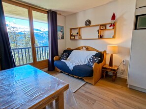 A cozy room with a wooden bed, a small bedside table, a lamp, and a view of the outdoors through a large window.