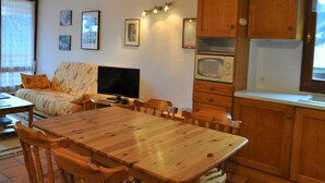 Un salon chaleureux avec une table à manger en bois, un canapé et un téléviseur. Des tableaux encadrés ornent le mur et il y a un four à micro-ondes dans le coin cuisine.