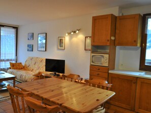 Una sala de estar acogedora con una mesa de comedor de madera, un sofá y un televisor. Hay cuadros enmarcados en la pared y un microondas en la cocina.