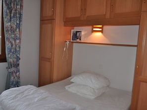 Un dormitorio con armarios de madera, una cama con ropa de cama blanca y una mesita de noche con lámpara.