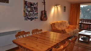 Un coin repas avec une table et des chaises en bois, une guitare et un mur orné d’un collage de photos.