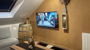 A room with a television mounted on the wall, a wooden barrel, a decorative vase, and a radiator. - La fine bulle! (Épernay)