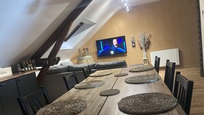 A dining area with a long wooden table, multiple woven placemats, and a television mounted on the wall. - La fine bulle! (Épernay)
