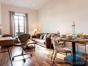 En moderne stue med et træspisebord dækket til fire personer, en lædersofa og et stort vindue med gardiner.