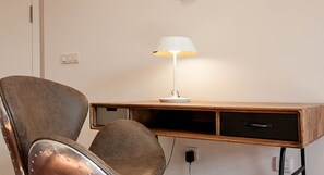 Una moderna sedia da ufficio con borchie metalliche, una scrivania in legno con una lampada e una presa di corrente.