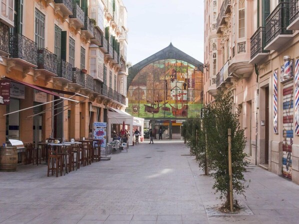 Une rue étroite, bordée de bâtiments des deux côtés, avec des terrasses de café et une grande fresque murale en arrière-plan.