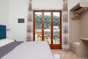 A bedroom with a bed, a wooden wardrobe, a balcony with a view of buildings and greenery. - Parsano suite (Sorrento)