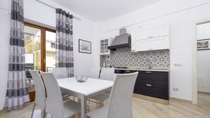 A modern kitchen with white cabinets, a patterned backsplash, and a dining area with a white table and chairs. - Parsano suite (Sorrento)
