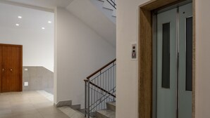 A modern interior with a wooden door, a staircase with metal railings, and a light blue elevator. - Parsano suite (Sorrento)