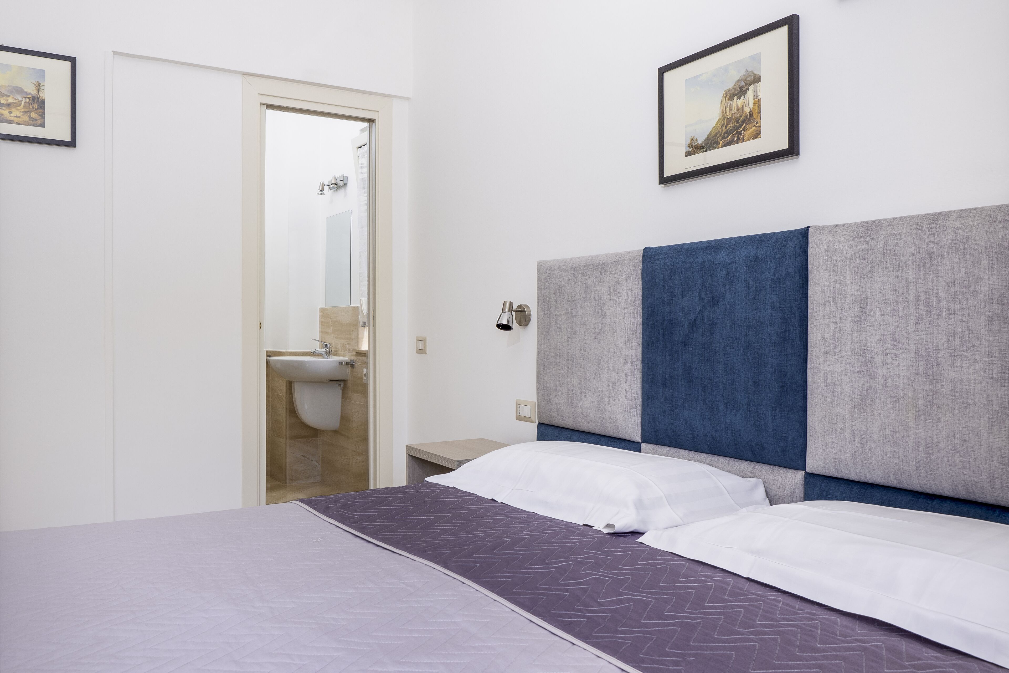 Ein Schlafzimmer mit Bett, Nachttisch, Wandlampe und einer Tür zu einem Badezimmer.