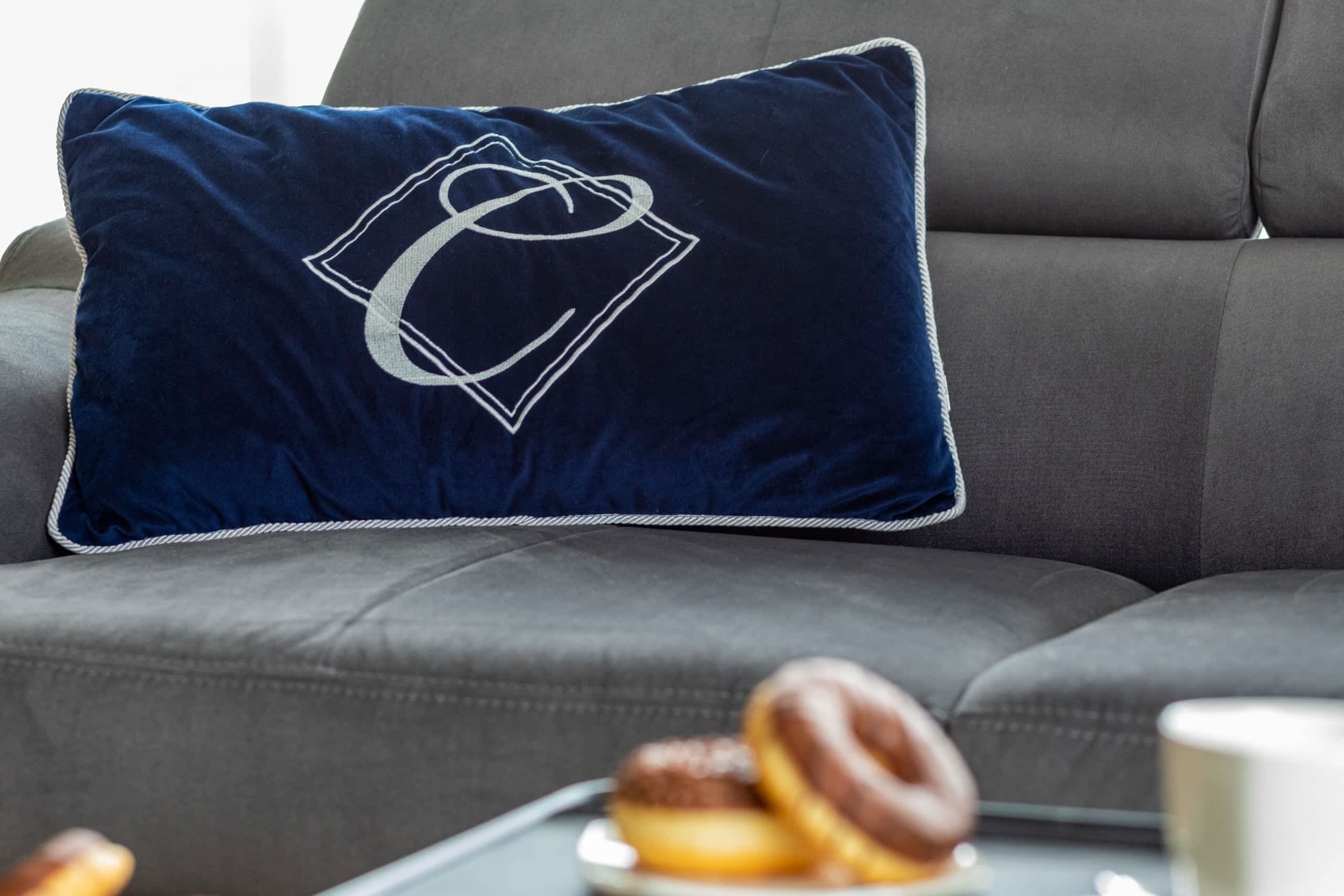 Un coussin bleu foncé orné d’un logo blanc, posé sur un canapé gris.