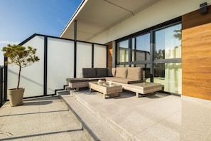 Un área de estar exterior moderna con sofá y mesa de centro, una planta en maceta y una escalera que conduce a un nivel superior.