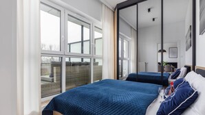 A modern hotel room with large windows, a bed with blue bedding, and a view of the outdoors.