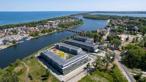 An aerial view of a modern building complex with multiple structures, a river, and surrounding greenery.